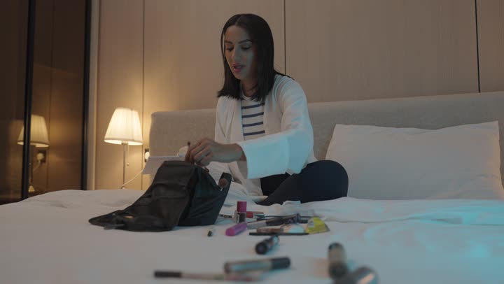 أدوات تجميل نسائيه عصريه، إمرأة عربية خليجية سعودية تجلس على السرير في غرفة النوم تقوم بوضع الميكاب، مفهوم الانوثه والاهتمام بالمظهر الخارجي, الاستعداد والتجهز للخروج