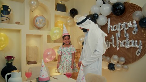 الفرحة والبهجة في المناسبات العائلية السعيدة، قضاء الأوقات الممتعه مع الأبناء، ايماءات وجه تدل على الإستمتاع والفرح، مفهوم الألفة والمحبة الأسرية، تصوير مقرب لاب عربي خليحي اماراتي يرتدي الثوب التقليدي يحتفل بعيد الميلاد مع  طفلته