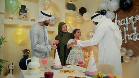 الزيارات العائلية وتجمعات الأسر، زينة ومفرقعات الحفلات، عائله عربيه خليجيه اماراتية ترتدي الثوب التقليدي تحتفل بعيد الميلاد مع  طفتلهم ،ايماءات وجه تدل على الإستمتاع والفرح، اب خليجي يقوم بالرقص مع ابنته