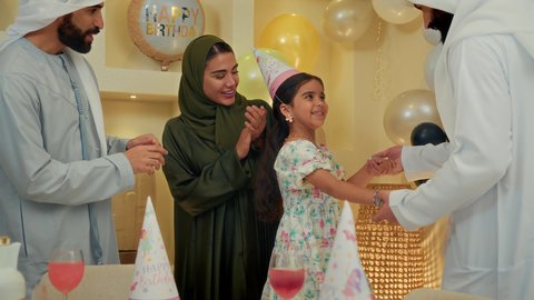 مشاركة لأجواء رائعة لعائلة اماراتية في المنزل ، زينة ومفرقعات الحفلات، عائله عربيه خليجيه اماراتية ترتدي الثوب التقليدي تحتفل بعيد الميلاد مع  طفتلهم ،ايماءات وجه تدل على الإستمتاع والفرح، اب خليجي يقوم بالرقص مع ابنته