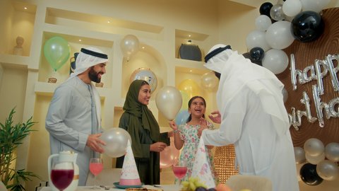 استقبال عائلي في المنزل، أجواء لمة الأهل في المناسبات والاحتفالات السعيدة ، زينة ومفرقعات الحفلات، عائله عربيه خليجيه اماراتية ترتدي الثوب التقليدي تحتفل بعيد الميلاد مع  طفتلهم ،ايماءات وجه تدل على الإستمتاع والفرح