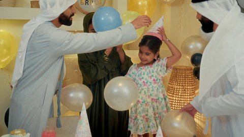 The atmosphere of family gatherings on happy occasions and celebrations, party decorations and fireworks, an Arab Gulf Emirati family wearing traditional dress celebrating a birthday with their child, facial expressions indicating enjoyment and joy