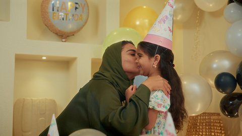 زينة ومفرقعات الحفلات، تعليق الزينة والبالونات الملونة، اعياد ومناسبات سعيدة، ايماءات السعاجة و السرور، ام عربيه خليجيه اماراتية تقوم بتقبيل ابنتها و الاحتفال بعيد ميلادها