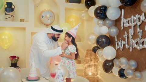 تعليق الزينة والبالونات الملونة، اعياد ومناسبات سعيدة، مشاركة لأجواء رائعة عائلية داخل المنزل، ام عربية خليجيه تقوم بحمل طفلتها للاعلي بايماءات السعادة و السرور، عائله عربيه خليجيه اماراتية تقوم بالاحتفال بعيد ميلاد ابنتهم