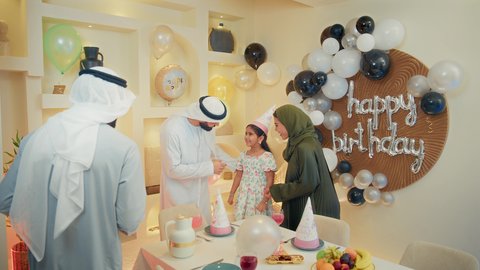 تقديم الهدايا في المناسبات والأعياد، مشاعر الحب والحنان في اجتماع عائلي سعيد، مشاركة لأجواء رائعة لعائلة اماراتية داخل المنزل،عائله عربيه خليجيه اماراتية ترتدي الزي التقليدي تقوم بالاحتفال بعيد ميلاد طفلتهم بايماءات السعادة و السرور