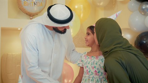 مشاعر الحب والحنان في اجتماع عائلي سعيد، مشاركة لأجواء رائعة لعائلة اماراتية داخل المنزل، تصويرمقرب لزوجان عربيان خليجيان اماراتيان يرتديان الزي التقليدي يقومان بالاحتفال بعيد ميلاد ابنتهم و تقبيلها