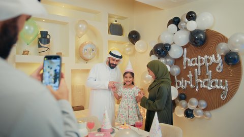مشاعر الحب والحنان في اجتماع عائلي سعيد، النظر الى الكاميرا بايماءات السرور والفرح، استخدام الأجهزة التقنية الحديثة، تقديم كعكة يوم الميلاد المزينة بالشموع , أسرة عربية خليجية اماراتية تقوم بالاحتفال بعيد الميلاد، اب عربي خليجي يقوم بأخذ صورة تذكارية من خلال الجوال