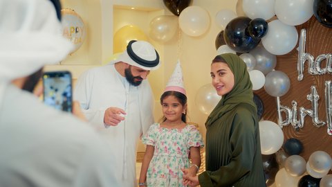 النظر الى الكاميرا بايماءات السرور والفرح، استخدام الأجهزة التقنية الحديثة، مشاعر الحب والحنان في اجتماع عائلي سعيد، تقديم كعكة يوم الميلاد المزينة بالشموع , أسرة عربية خليجية اماراتية تقوم بالاحتفال بعيد الميلاد، اب عربي خليجي يقوم بأخذ صورة تذكارية من خلال الجوال