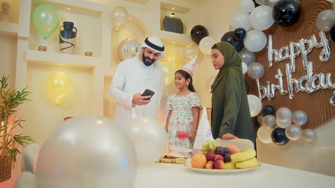 استخدام الأجهزة التقنية الحديثة، مشاعر الحب والحنان في اجتماع عائلي سعيد، تقديم كعكة يوم الميلاد المزينة بالشموع , أسرة عربية خليجية اماراتية تقوم بالاحتفال بعيد الميلاد، اب عربي خليجي يقوم بأخذ صورة تذكارية من خلال الجوال, النظر الى الكاميرا بايماءات السرور والفرح