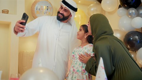مشاعر الحب والحنان في اجتماع عائلي سعيد، تقديم كعكة يوم الميلاد المزينة بالشموع , أسرة عربية خليجية اماراتية تقوم بالاحتفال بعيد الميلاد، اب عربي خليجي يقوم بأخذ صورة تذكارية من خلال الجوال, النظر الى الكاميرا بايماءات السرور والفرح