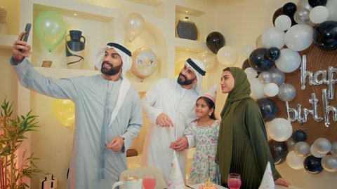 تقديم كعكة يوم الميلاد المزينة بالشموع , أسرة عربية خليجية اماراتية تقوم بالاحتفال بعيد الميلاد، أخذ صورة تذكارية من خلال الجوال، مشاعر الحب والحنان في اجتماع عائلي سعيد, النظر الى الكاميرا بايماءات السرور والفرح