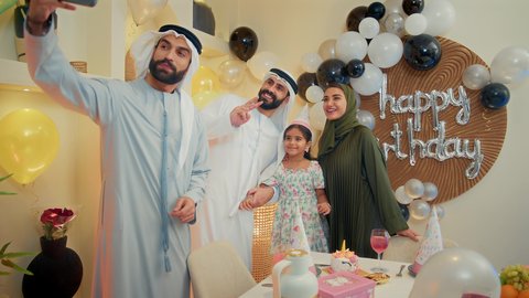 الاحتفال بالمناسبات والأعياد بأجواء عائلية سعيدة, أسرة عربية خليجية اماراتية تقوم بالاحتفال بعيد الميلاد، أخذ صورة تذكارية من خلال الجوال مع الكعكة المزينة بالشموع، مشاعر الحب والحنان في اجتماع عائلي سعيد, النظر الى الكاميرا بايماءات السرور والفرح