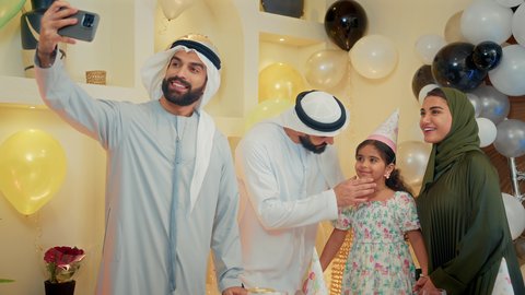 التقاط صور السيلفي التذكارية من خلال الجوال، زينة أعياد الميلاد و المناسبات ، عائله عربيه خليجيه اماراتية ترتدي الزي التقليدي تحتفل بعيد ميلاد ابنتهم  ، كيكة عيد ميلاد مع الشموع ، الاستمتاع و الترفيه ، مناسبات عائلية سعيدة