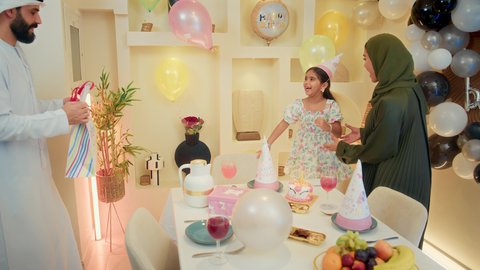 ذكريات رائعه مع الأبناء، ايماءات المفجاء و الاندهاش ، اب عربي خليجي يقوم بتقديم الهديه لابنته ، عائله عربيه خليجيه اماراتية ترتدي الزي التقليدي تقوم بالاحتفال بعيد ميلاد ابنتهم، مفهوم الأسرة والطفل، قضاء أوقات عائلية ممتعة