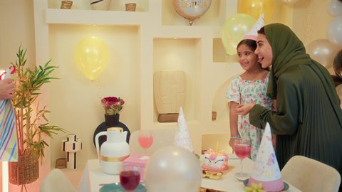 الاستمتاع و الترفيه بأجواء الاحتفالات، ايماءات المفجاء و الاندهاش ، اب عربي خليجي يقوم بتقديم الهديه لابنته ، عائله عربيه خليجيه اماراتية ترتدي الزي التقليدي تقوم بالاحتفال بعيد ميلاد ابنتهم، مفهوم الأسرة والطفل، قضاء أوقات عائلية ممتعة