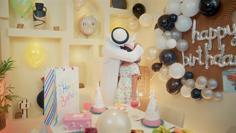 أجواء مليئة بالحب، ايماءات المفجاء و الاندهاش ، ام خليجيه تقوم بتقديم الهديه لابنتها ، عائله عربيه خليجيه اماراتية ترتدي الزي التقليدي تقوم بالاحتفال بعيد ميلاد ابنتهم، مفهوم الأسرة والطفل، قضاء أوقات عائلية ممتعة