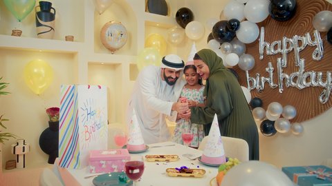 كيكة عيد ميلاد مع الشموع ، تعليق الزينة والبالونات الملونة ، عائله عربيه خليجيه اماراتية ترتدي الزي التقليدي تقوم بالاحتفال بعيد ميلاد ابنتهم ، الاستمتاع و الترفيه ، مناسبات عائلية سعيدة