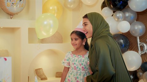 تعليق الزينة والبالونات الملونة، إيماءات السعادة والمفجاءة،  استقبال الهدايا من الحضور والأهل، الاحتفال بأعياد الميلاد في أجواء عائلية دافئة، طفلة عربية خليجية اماراتية ترتدي فستان تحتفل بعيد ميلادها برفقة أسرتها