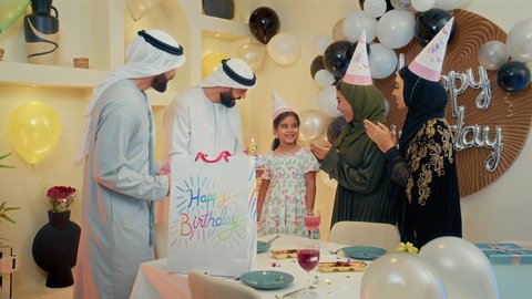 أجواء سعيدة لأسرة اماراتية،عائله عربيه خليجيه اماراتية يرتدون الملابس التقليدية يقومان بالاحتفال بعيد ميلاد ابنتهما الصغيرة، فتاة ترتدي فستان ملون تقوم باطفاء شمعه كيكه العيد ميلاد بايماءات السعادة و السرور
