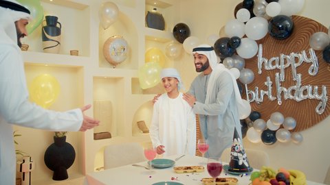 مفهوم المحبة والألفة بين أفراد العائلة، تعليق الزينة والبالونات الملونة واكسسوارات الحفل، عائله عربيه خليجيه اماراتية تقوم بالاحتفال بعيد الميلاد، رجل عربي خليجي اماراتي يرتدي الزي التقليدي يقوم بتقبيل الولد ، ايماءات السعادة و السرور
