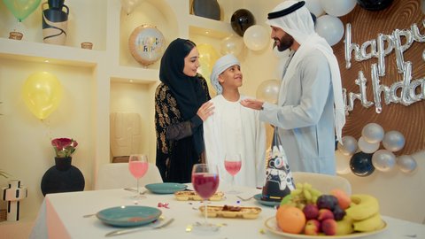 أعياد ومناسبات عائلية سعيدة، زينة أعياد الميلاد و المناسبات ، الاستمتاع و الترفيه ،عائله عربيه خليجيه اماراتية تقوم بالاحتفال بولدهم ، اب عربي خليجي اماراتي يرتدي الزي التقليدي يقوم بتقبيل ابنه ، مفهوم الإهداء والتقدير، ايماءات السعادة و السرور