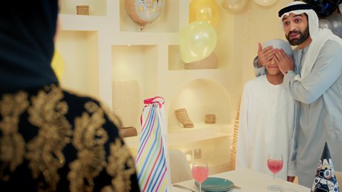 Celebrating birthdays, expressing love and appreciation, a family atmosphere full of intimacy, balloons and a birthday cake decorated with candles, an Arab Gulf Emirati family spending fun times at home, an Arab Gulf Emirati mother surprises and presents a gift to her son