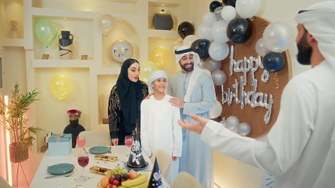 فن تقديم الهدايا، مشاركة وتقديم الهدايا بالمناسبات وأعياد الميلاد، مشاعر الحب والحنان في اجتماع عائلي سعيد, أجواء أسرية مليئة بالألفة، بلالين وكعكة يوم الميلاد المزينة بالشموع، عائلة عربية خليجية إماراتية تقضي أوقات ممتعه في المنزل، إيماءات الفرح و السعادة