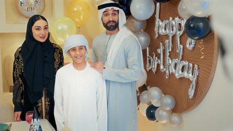 احتفال عائلي بسيط في المنزل، مشاركة وتقديم الهدايا بالمناسبات وأعياد الميلاد، مشاعر الحب والحنان , أجواء أسرية مليئة بالألفة، بلالين وكعكة يوم الميلاد المزينة بالشموع، عائلة عربية خليجية إماراتية تقوم بالاحتفال بأبنهم، إيماءات الفرح و السعادة