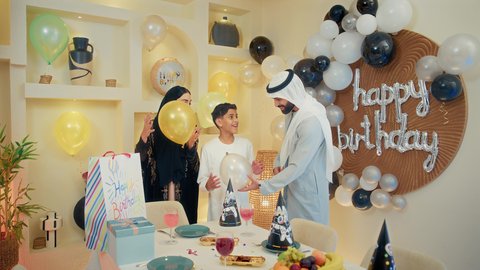 البهجة والفرحة في المناسبات العائلية السعيدة، مشاركة وتقديم الهدايا بالمناسبات وأعياد الميلاد، مشاعر الحب والحنان في اجتماع عائلي سعيد, أجواء أسرية مليئة بالألفة، بلالين وكعكة يوم الميلاد المزينة بالشموع، عائلة عربية خليجية إماراتية تقضي أوقات ممتعه في المنزل، إيماءات الفرح و السعادة