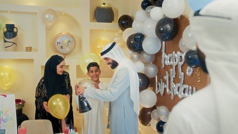 أجواء مليئة بالتقدير والاحترام، مشاركة وتقديم الهدايا بالمناسبات وأعياد الميلاد، مشاعر الحب والحنان في اجتماع عائلي سعيد, أجواء أسرية مليئة بالألفة، بلالين وكعكة يوم الميلاد المزينة بالشموع، عائلة عربية خليجية إماراتية تقضي أوقات ممتعه في المنزل، إيماءات الفرح و السعادة