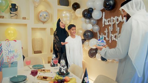 تعزيز روابط الأبوة والحنان ، أجواء فرحة لعائلة امارتية، الاحتفال بأعياد ميلاد الأطفال، الاستمتاع و الترفيه ، مناسبات عائلية سعيدة، اب عربي خليجي اماراتي يحمل كيكة عيد ميلاد مع الشموع يقوم بتقبيل ابنه ، مفهوم الإهداء والتقدير