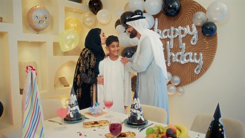 مفهوم أهمية الأسرة، زوجان عربيان خليجيان اماراتيان يرتديان الزي التقليدي يقومان بتقبيل ابنهم، عائلة عربية خليجية إماراتية تقوم بالاحتفال بعيد الميلاد، إيماءات الفرح و السعادة، مشاعر الحب والحنان في اجتماع عائلي سعيد