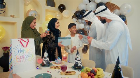 تعزيز الروابط العائلية والمحبة والمودة بين الأسرة، الاستمتاع بالاحتفال بعيد ميلاد الابن، عائلة عربية خليجية إماراتية تقوم بالاحتفال و تقديم الهدايا، إيماءات الفرح و السعادة، مشاعر الحب والحنان في اجتماع عائلي سعيد