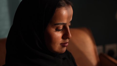 مهنة ووظيفة مكتبية، انجاز وادارة المهام باستخدام جهاز تقني حديث ومتطور, إمرأة عربية خليجية سعودية مبتسمة ترتدي الحجاب والعباءة وتجلس على الكنبة تعمل على جهاز التابلت في صالة المنزل