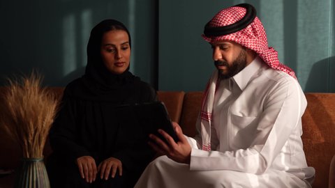 الحوار و النقاش بين الزملاء، بيئة العمل المريحة في الشركات السعودية، تبادل الخبرات والمعلومات لتحقيق الاهداف, موظفان عربيان خليجيان سعوديان يعملان في صالة المنزل، استخدام الجهاز اللوحي في مجال الاعمال