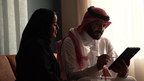 الحوار و النقاش بين الزملاء، بيئة العمل المريحة في الشركات السعودية، تبادل الخبرات والمعلومات لتحقيق الاهداف, موظفان عربيان خليجيان سعوديان يعملان في صالة المنزل، استخدام الجهاز اللوحي في مجال الاعمال