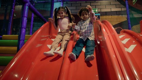 تصوير لطفلان عربيان خليجيان إماراتيان برتديان الزى الكاجوال ، يستمتعان بالانزلاق على زحليقة كبيرة ، الأنشطة الرياضية الممتعة ، مركز العاب ترفيهي داخلي ، أجواء حيوية ومبهجة، قضاء اوقات سعيدة