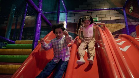 الأنشطة الرياضية الممتعة ، مركز العاب ترفيهي داخلي ، أجواء حيوية ومبهجة، قضاء اوقات سعيدة ، تصوير لطفلان عربيان خليجيان إماراتيان برتديان الزى الكاجوال ، يستمتعان بالانزلاق على زحليقة كبيرة