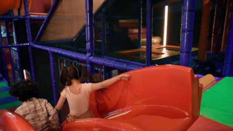 أجواء حيوية ومبهجة، قضاء اوقات سعيدة ، مركز العاب ترفيهي داخلي ،  تصوير لطفلان عربيان خليجيان إماراتيان برتديان الزى الكاجوال ، يستمتعون بالانزلاق على زحليقة كبيرة ، الأنشطة الرياضية الممتعة