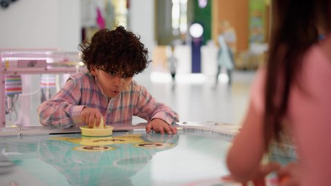 ايماءات الاندماج والتفاعل ، قضاء الاوقات السعيدة مع العائلة، الأنشطة الرياضية الممتعة ، منافسة مليئة بالتحدي والإثارة ،  تصوير لطفلان اشقاء عربيان خليجيان إماراتيان يرتديان الزى الكاجوال ، يستمتعان بلعبة الهوكي الهوائي