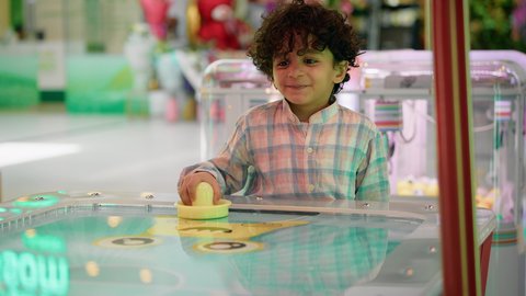 Gestures of integration and interaction, challenging and exciting competition, fun sports activities, a photo of an Emirati Gulf Arab child wearing casual clothes, enjoying a game of air hockey, having a good time.