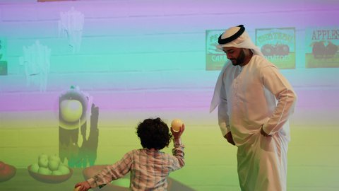 أجواء تفاعلية مبهجة ، مركز ألعاب ترفيهي، تعابير السرور والسعادة، مشاركة الأب ابنائه لحظات المرح والحماس ،  قضاء الاوقات السعيده مع الابناء ، تصوير لعائلة عربية خليجية إماراتية تستمتع بوقت ممتع في لعبة الرمي التفاعلية