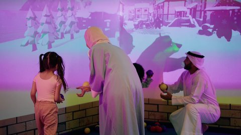 Entertainment games center, expressions of joy and happiness, father and mother sharing moments of fun and excitement with their children, spending happy times with the children, a cheerful interactive atmosphere, a photo of an Arab Gulf Emirati family enjoying a fun time in the interactive throwing game