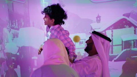 A photo of an Emirati Gulf Arab family having a fun time playing an interactive throwing game, enjoying moments of fun and excitement, a cheerful interactive atmosphere, an entertainment games center, expressions of pleasure and happiness, spending happy times with the children