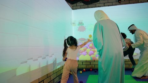 أجواء تفاعلية مبهجة ، قضاء الاوقات السعيده مع الابناء ، تصوير لعائلة عربية خليجية إماراتية تستمتع بوقت ممتع في لعبة الرمي التفاعلية ، مركز ألعاب ترفيهي، مشاركة الأب والأم أطفالهما لحظات المرح والحماس ، تعابير السرور والسعادة