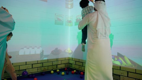 مشاركة الأب والأم أطفالهما لحظات المرح والحماس ، تعابير السرور والسعادة، تصوير لعائلة عربية خليجية إماراتية تستمتع بوقت ممتع في لعبة الرمي التفاعلية ، مركز ألعاب ترفيهي، أجواء تفاعلية مبهجة ، قضاء الاوقات السعيده مع الابناء