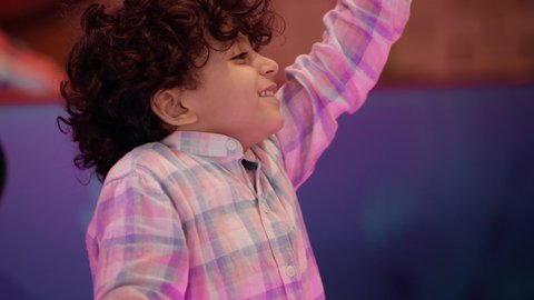 ايماءات الفوز والحماس والانتصار، قضاء اوقات ممتعه ، تصوير لطفل عربي خليجي إماراتي يرتدي الزى الكاجوال ، يستمتع بالانشطه الترفيهية فى احدي مراكز الالعاب فى الامارات