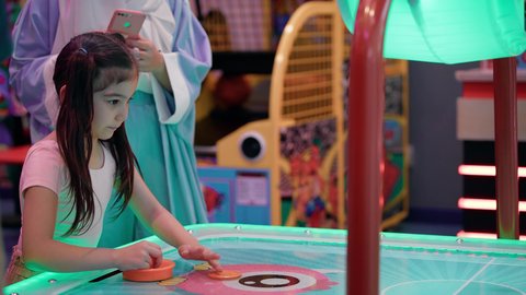 مراكز الالعاب الترفيهيه في الامارات، امراه اماراتيه توثق اللحظات التذكاريه السعيده لابنتها ،طاولة مضيئة بألوان زاهية ، قضاء اوقات ممتعه مع العائله ،  تصوير لطفلة عربية خليجية إماراتية ترتدي الزى الكاجوال ، تستمتع بلعب الهوكي الهوائي