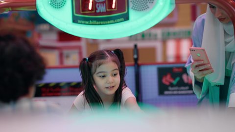 امراه اماراتيه توثق اللحظات التذكاريه السعيده لابنائها ،طاولة مضيئة بألوان زاهية ، قضاء اوقات ممتعه مع العائله ، مراكز الالعاب الترفيهيه في الامارات، تصوير لعائلة عربية خليجية إماراتية ترتدي الزى الكاجوال ، تستمتع بلعب الهوكي الهوائي ، ايماءات التحدي والحماس