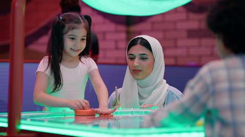 طاولة مضيئة بألوان زاهية ، قضاء اوقات ممتعه مع العائله ،ايماءات التحدي والحماس، مراكز الالعاب الترفيهيه في الامارات، تصوير لعائلة عربية خليجية إماراتية ترتدي الزى الكاجوال ، تستمتع بلعب الهوكي الهوائي